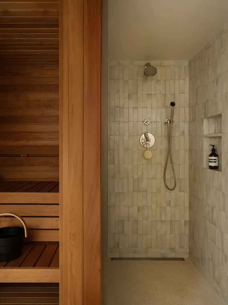 Shower niche with rainfall head and handheld fixture adjacent to timber sauna with slatted benches
