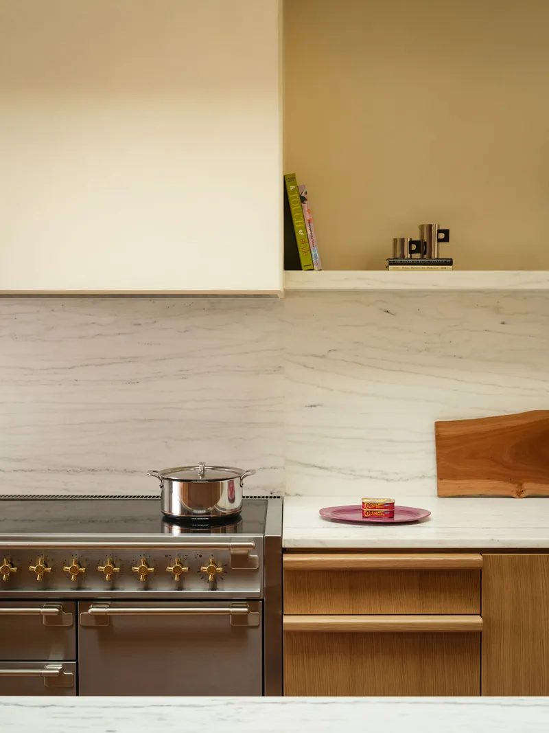 Kitchen counter with white marble backsplash, oak cabinetry and stainless range with brass knobs