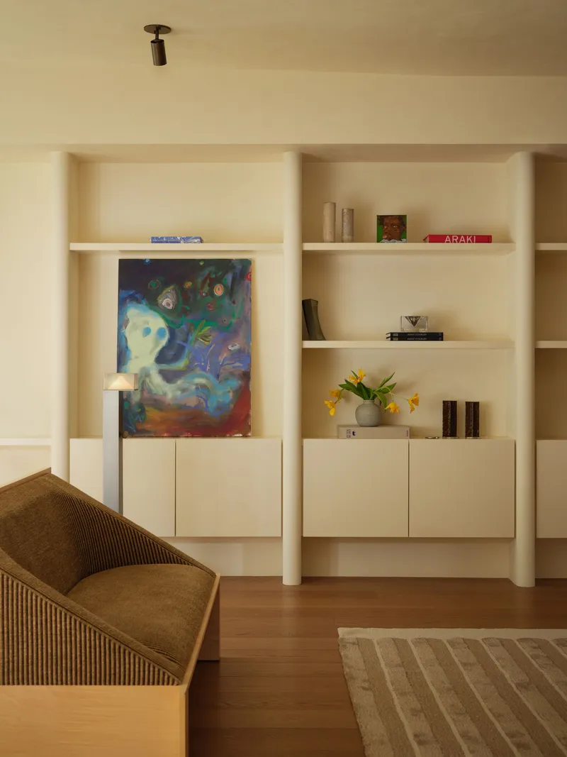 Built-in shelving unit with cylindrical columns, closed cabinetry and painting propped against the wall