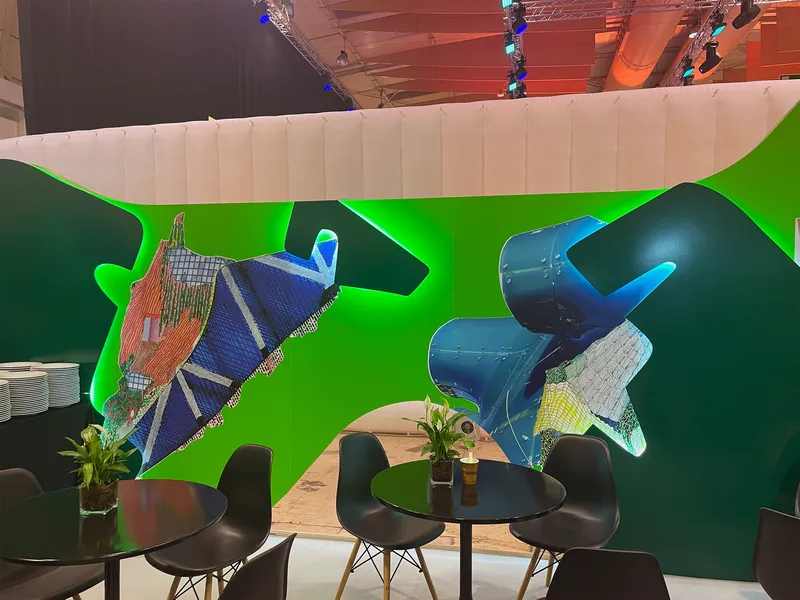 Green booth wall displaying architectural model collages above black chairs and round tables