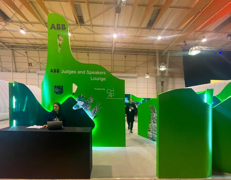 Exhibition booth with glossy green undulating partition walls and a reception desk under timber ceiling panels