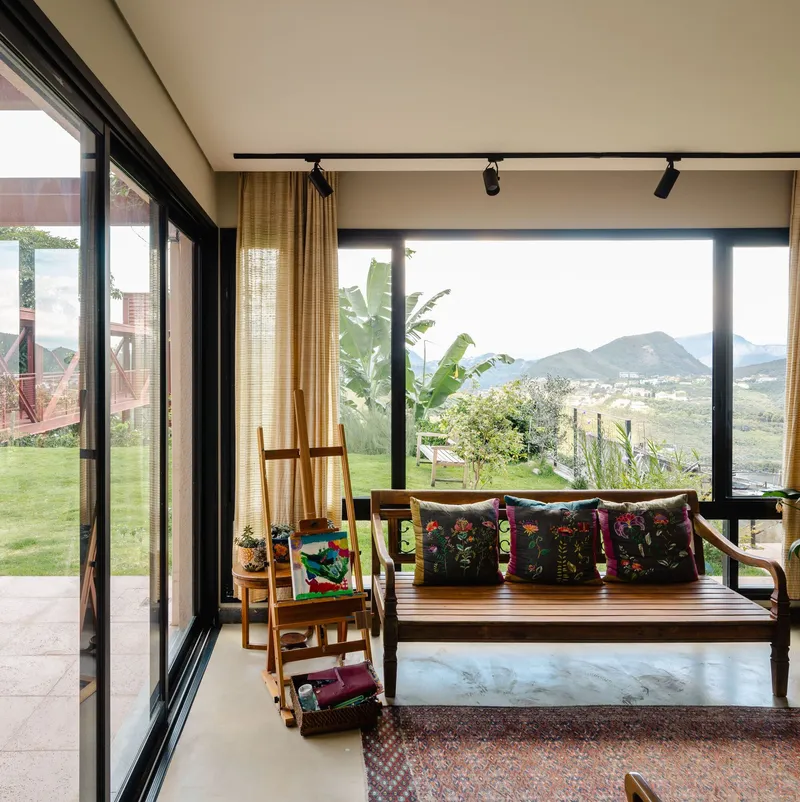 Corner window seat overlooking terraced hillside landscape through floor-to-ceiling black-framed glazing