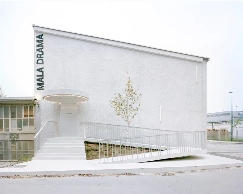 White rendered entrance facade with elevated walkway, circular canopy ring and single leafless sapling