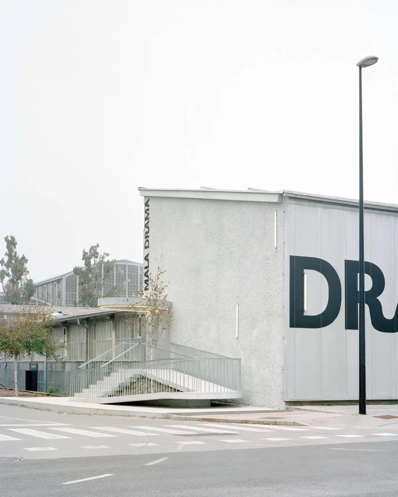 Street view of the white stucco volume with elevated ramp and large graphic lettering on wall