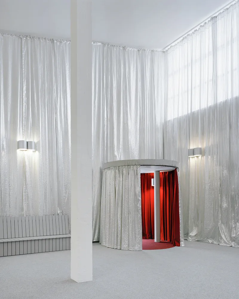 White foyer with silvery curtain walls surrounding a cylindrical enclosure with red drapes at its opening