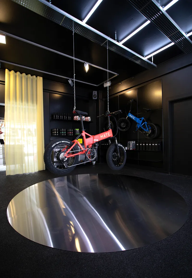 Suspended bicycles hanging above a circular polished steel floor disc with perforated black ceiling panels