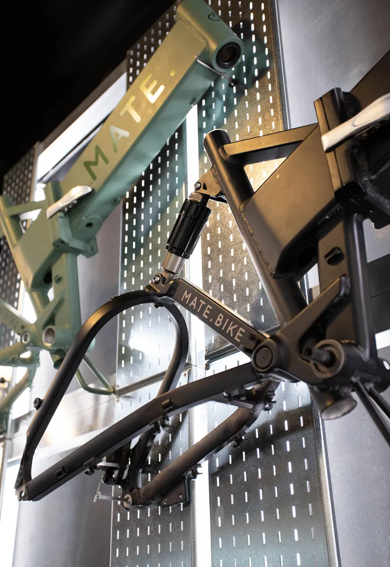 Close-up of folding bicycle frames suspended by chains against a perforated metal wall with backlighting