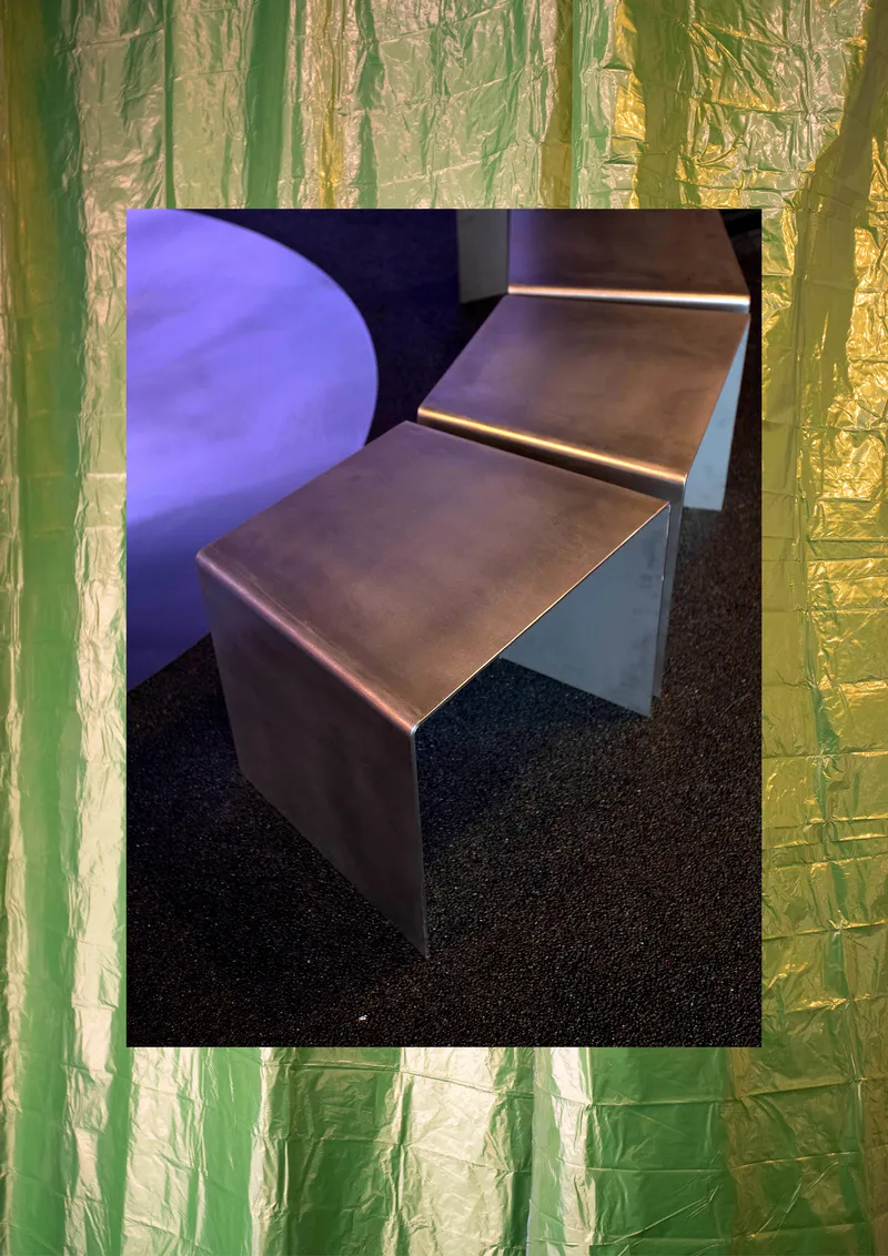 Angular metal bench framed by green and gold foil curtains with a purple circular element visible