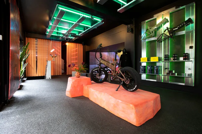 Interior showroom with orange foam display podium beneath green neon ceiling panels and corrugated orange partitions