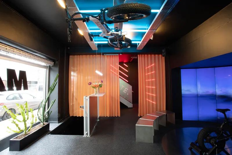 Entry view through storefront glazing showing corrugated orange dividers and blue neon ceiling lights
