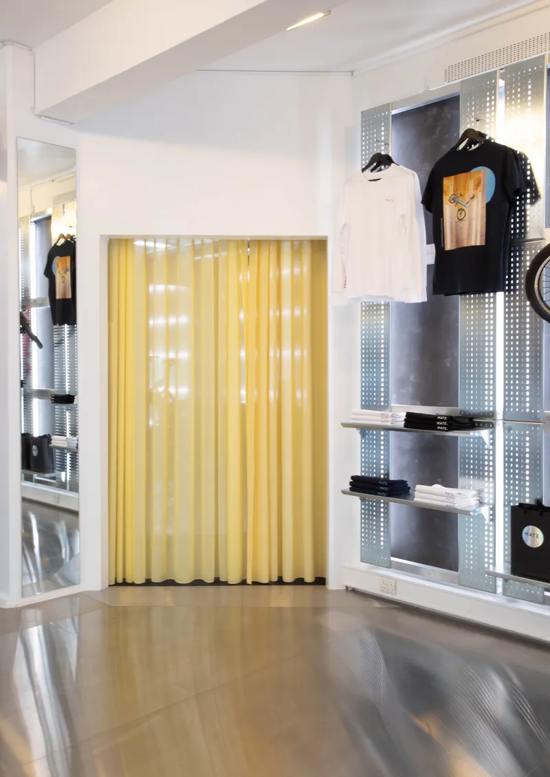 Retail wall with perforated metal shelving and merchandise behind translucent yellow curtain