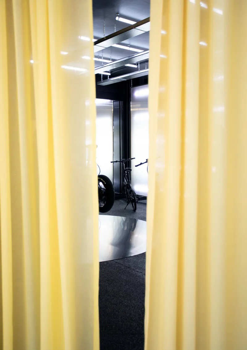 View through yellow pleated curtains into showroom space with exposed ceiling and black floor