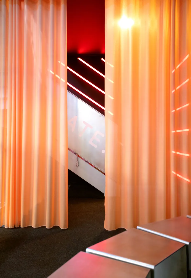 Passageway framed by orange backlit curtains with horizontal light strips in the distance