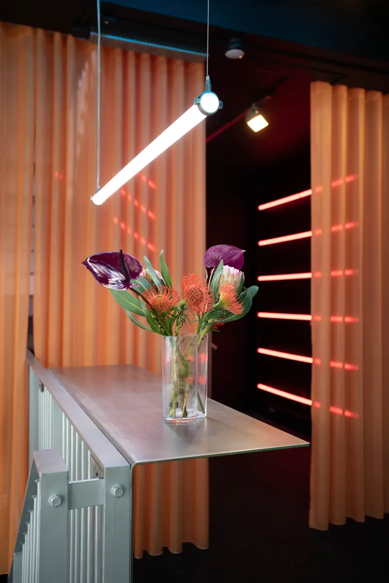 Glass vase with protea and anthurium flowers on a pale display table under pendant lighting