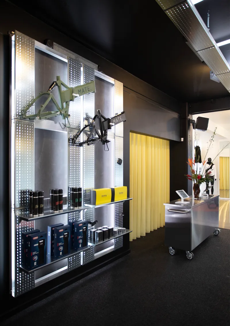 Backlit perforated metal display wall with shelving and suspended bikes in a dark retail interior