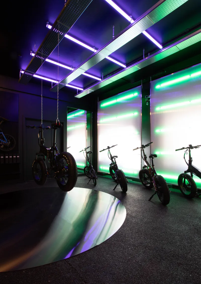 Display room with suspended linear lighting in purple and green illuminating a row of bikes