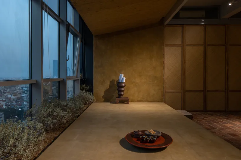Window bay with planted bed and sculpture beside woven storage wall at dusk