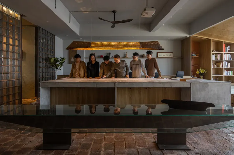 Interior workspace with staff gathered around a concrete counter beneath a woven timber pendant light