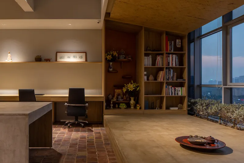 Workspace at dusk with bookshelf niche and floor-to-ceiling windows revealing twilight cityscape