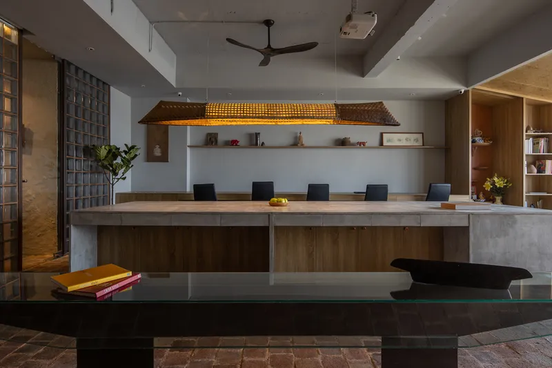 Dining and workspace with timber table, woven pendant light and reclaimed brick flooring beneath a stepped ceiling