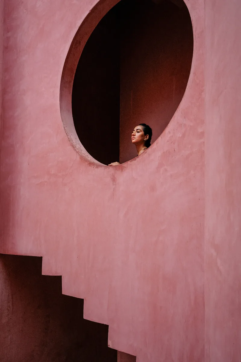 Oval opening in a pink plastered wall with a figure looking out and a staircase below
