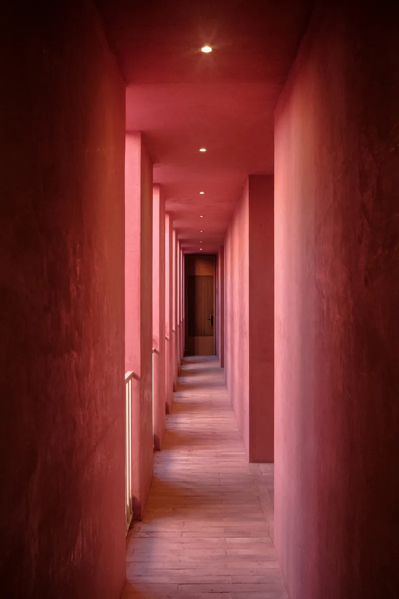 Long corridor with pink plaster walls, recessed ceiling lights and timber flooring stretching into the distance