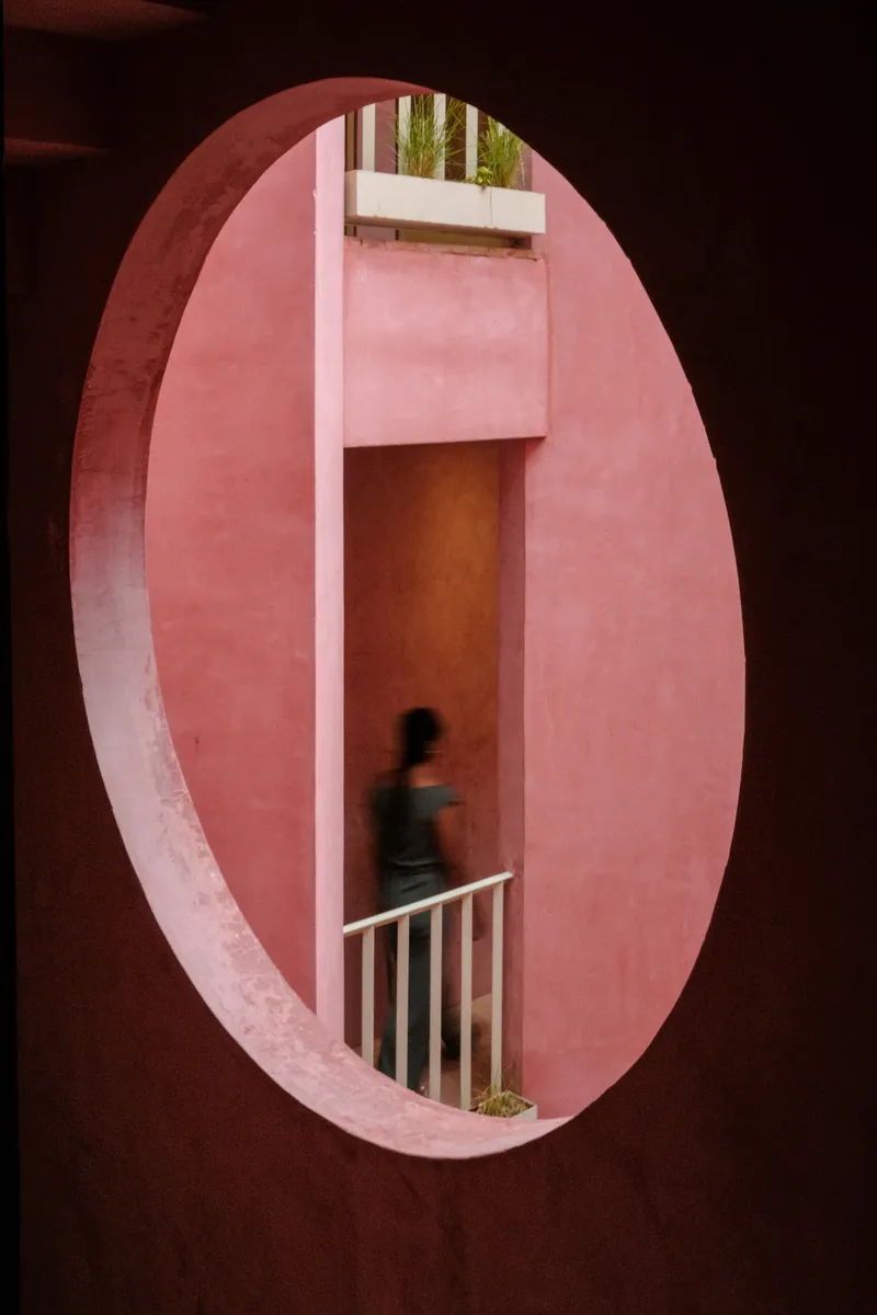 View through an oval aperture revealing interior stairwell with white railing and planted terrace above