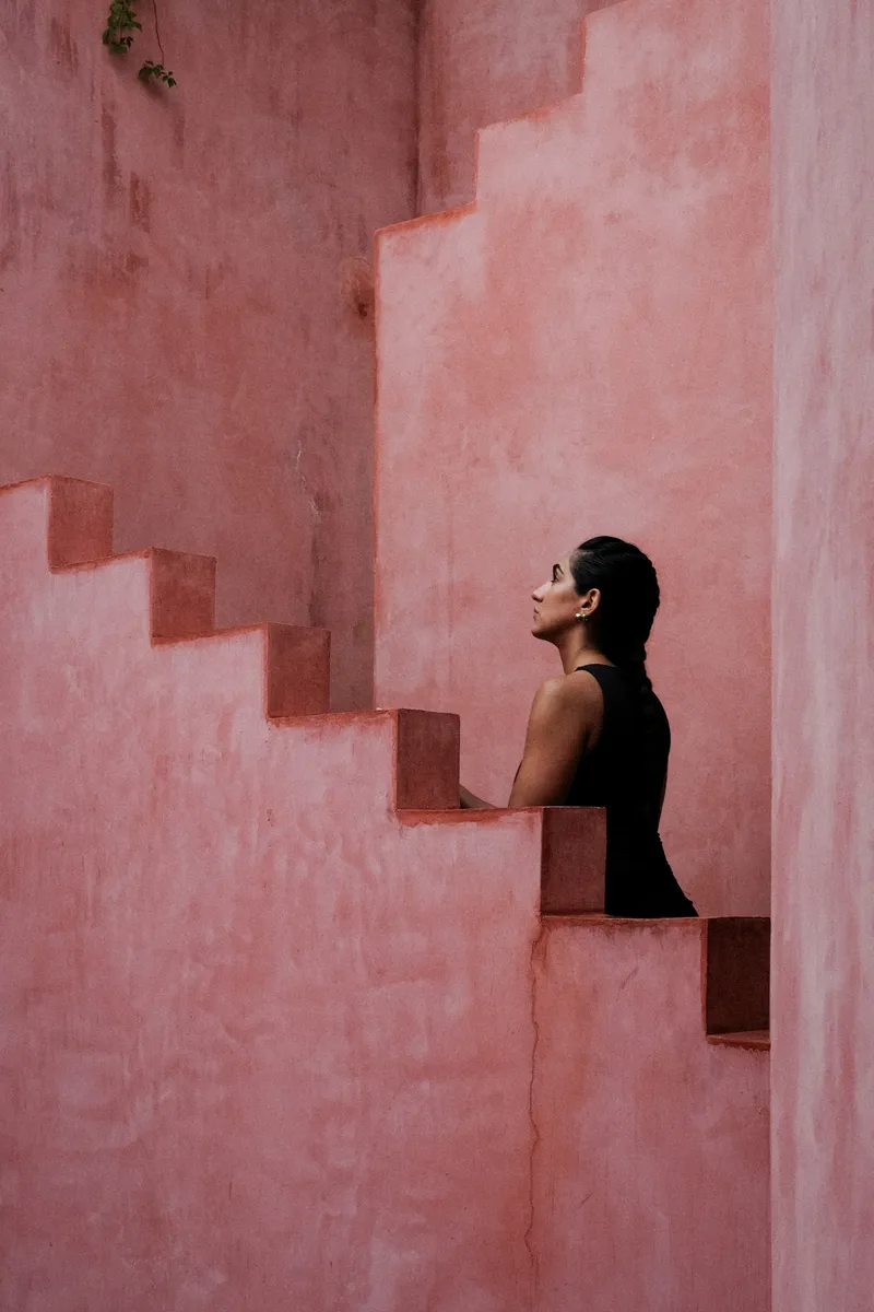 Cantilevered pink plaster steps emerging from corner walls with a person looking upward