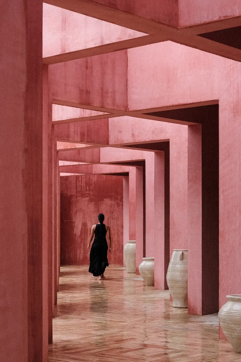 Enfilade of nested pink plaster doorways with person walking past ceramic vessels on polished floor