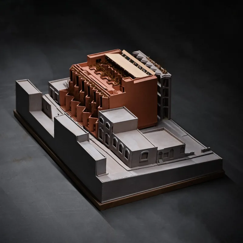 Physical model showing sawtooth roofline and courtyard surrounded by white and copper-toned volumes on a black base