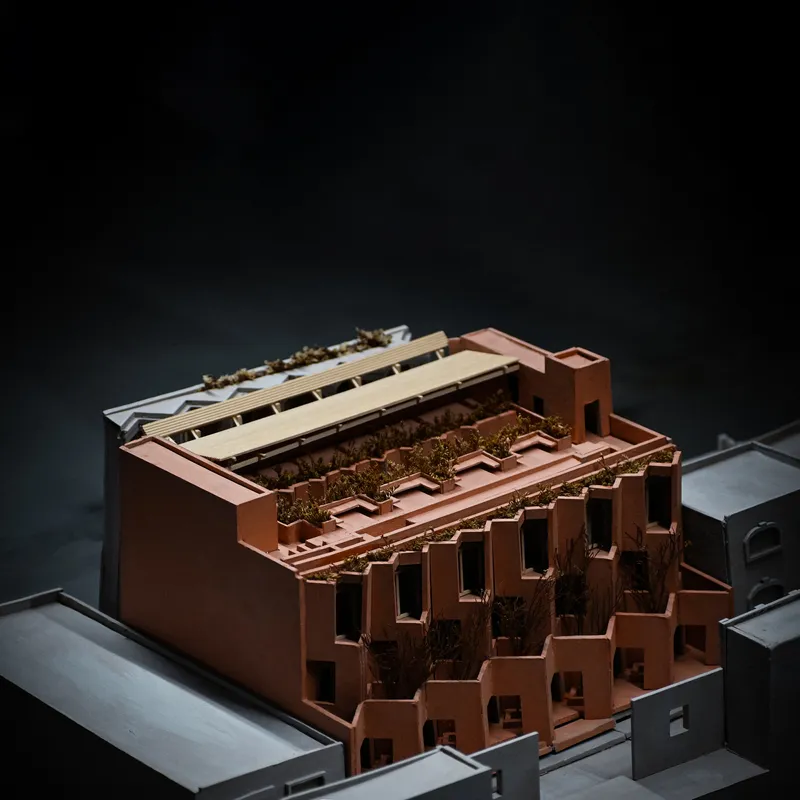 Physical model showing terraced copper facades with planted trees along stepped massing in dramatic lighting