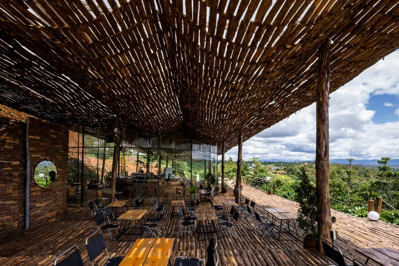 Dining area beneath a curved lattice roof supported by rustic timber posts with views to distant hills
