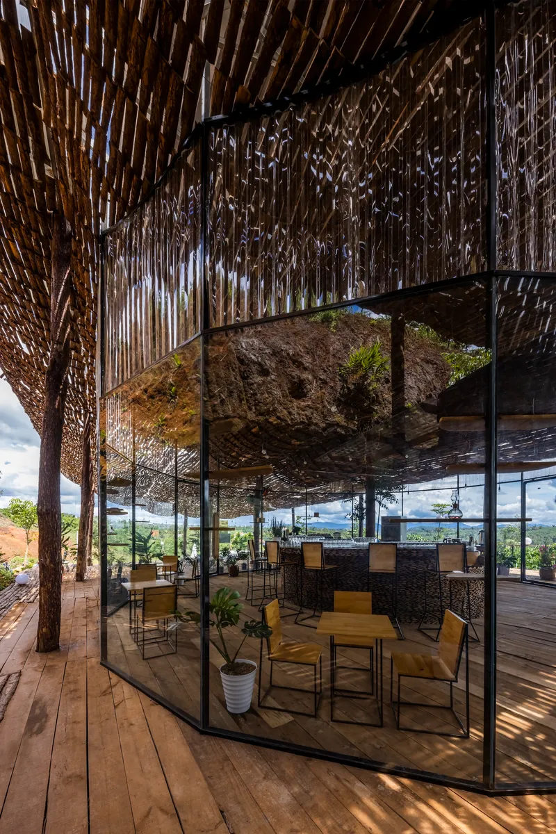 Glass-enclosed lounge area with a suspended rock feature beneath the timber lattice roof structure