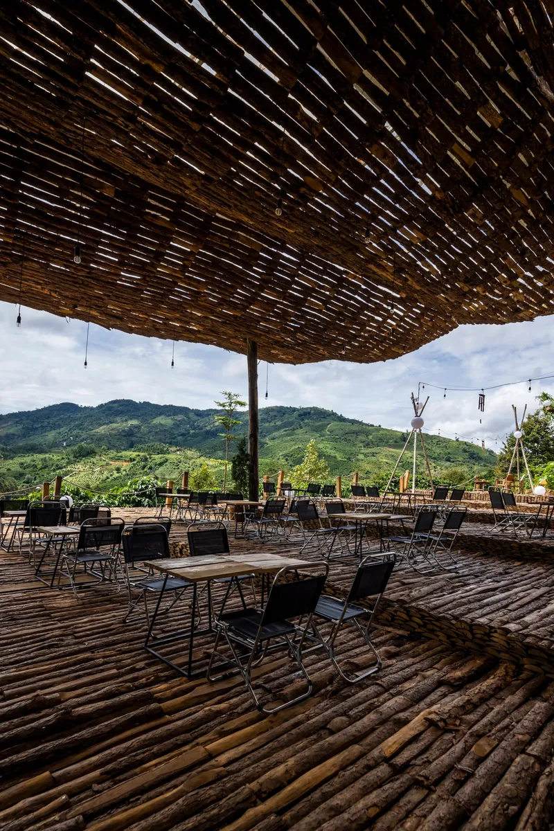 Outdoor dining area beneath woven bamboo canopy on split bamboo flooring with mountain backdrop