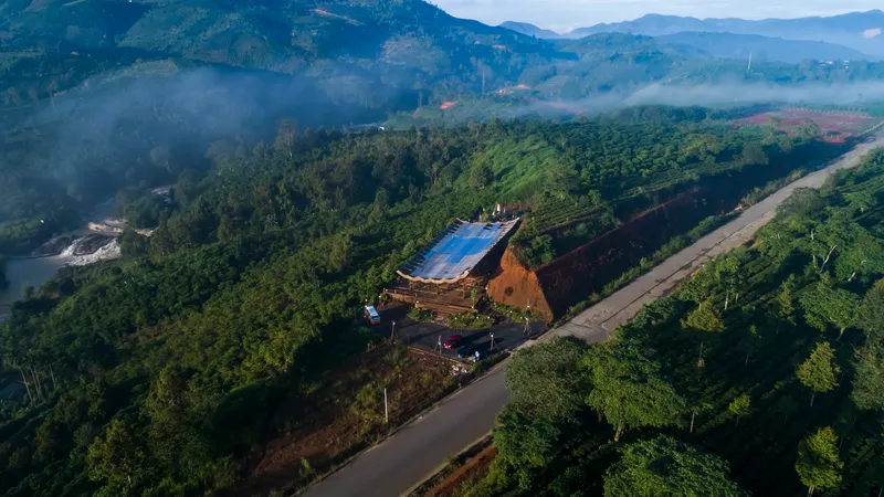 Aerial view of the compound on a forested ridgeline with morning mist in the valley below