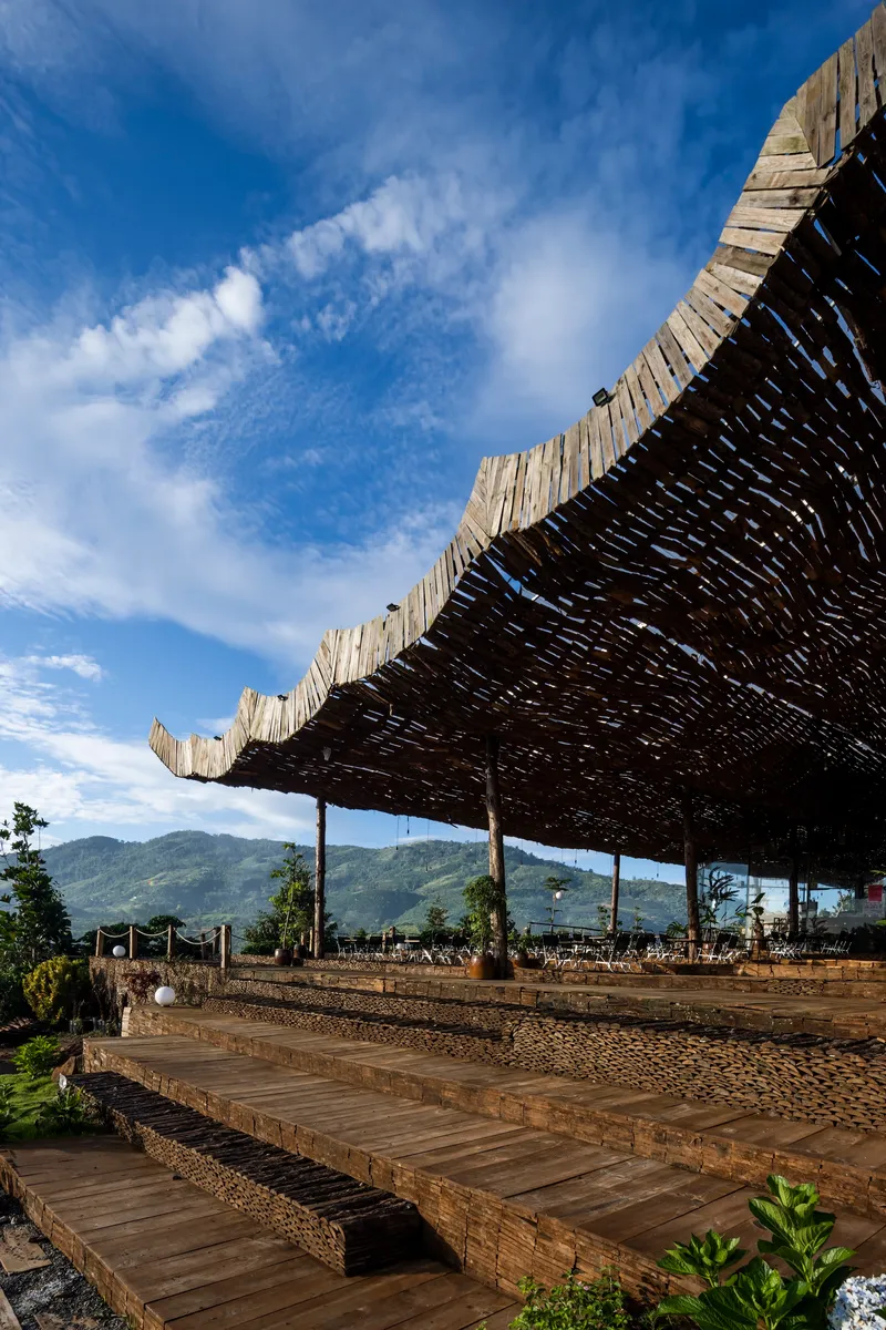 Stepped timber platforms leading up to the woven bamboo roof structure against distant green peaks