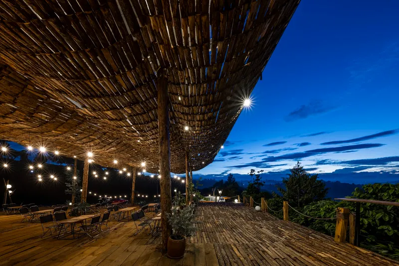 Terrace with string lights beneath bamboo canopy at dusk with distant mountains
