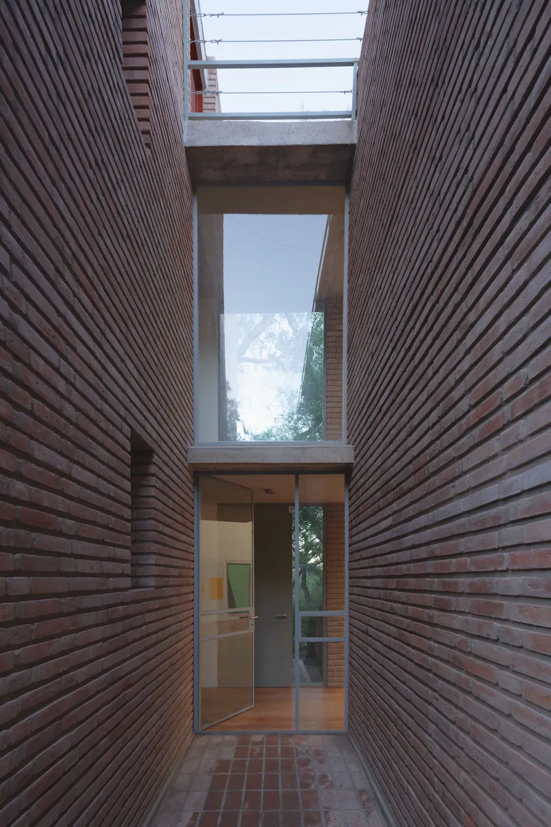 Narrow brick-paved courtyard between horizontal timber-clad walls leading to glazed doors and skylight opening above