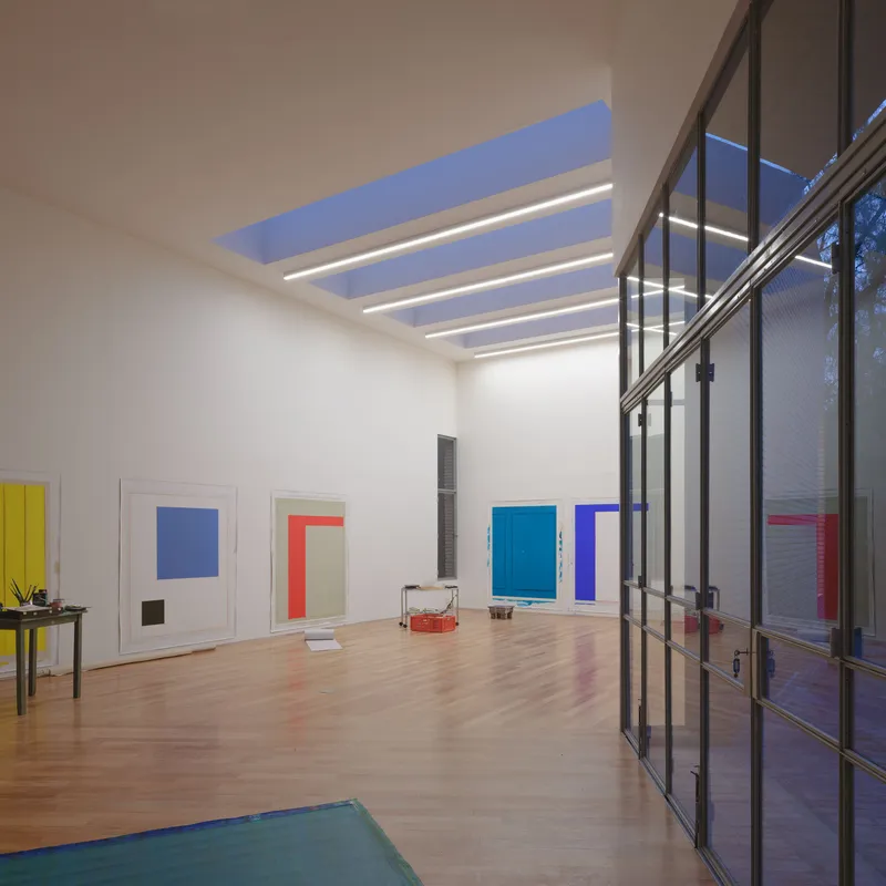 Studio interior at dusk with skylight bands glowing above and steel-framed glass doors opening to courtyard