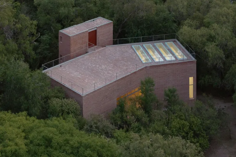 Aerial view of the brick structure with flat roof and clerestory windows surrounded by forested hillside