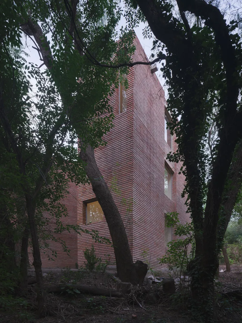 Vertical brick tower with triangular window opening rising through overhanging tree branches
