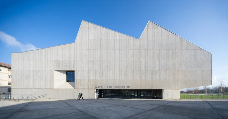 Front elevation of the vertically ribbed facade with recessed entrance and pedestrians crossing the forecourt