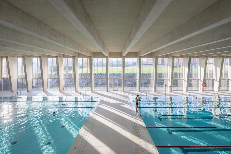 Indoor swimming pool with exposed concrete beams and ribbon windows overlooking an open field