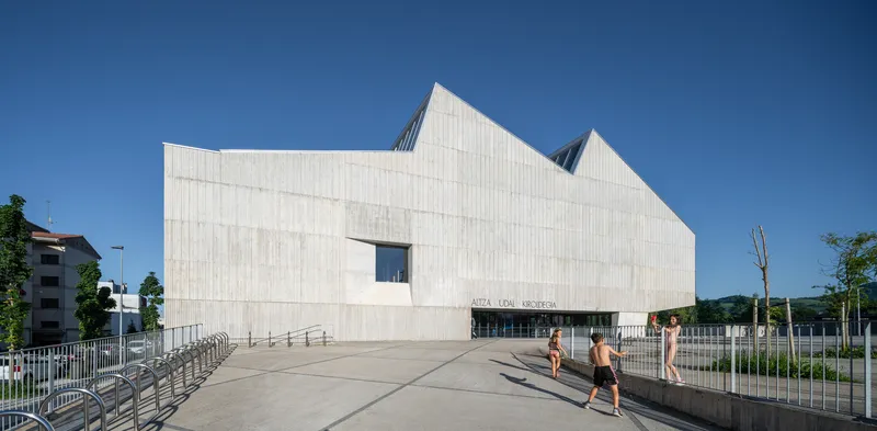 Entrance facade with single punched window above the glazed entry and metal railings in afternoon sun
