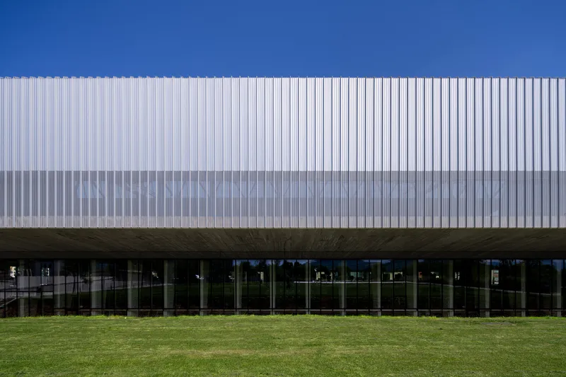 Elevated volume clad in vertical white metal fins above a glazed ground floor and lawn