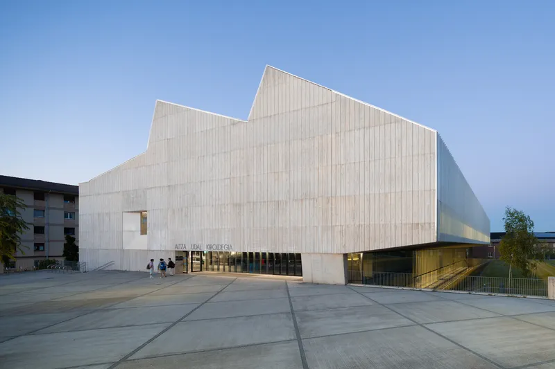 Street view of the faceted concrete volume with small square window at dusk