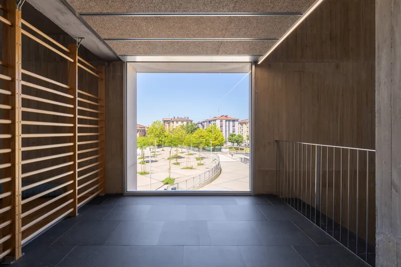 Timber-lined passageway framing a view of the tree-lined plaza through a square opening