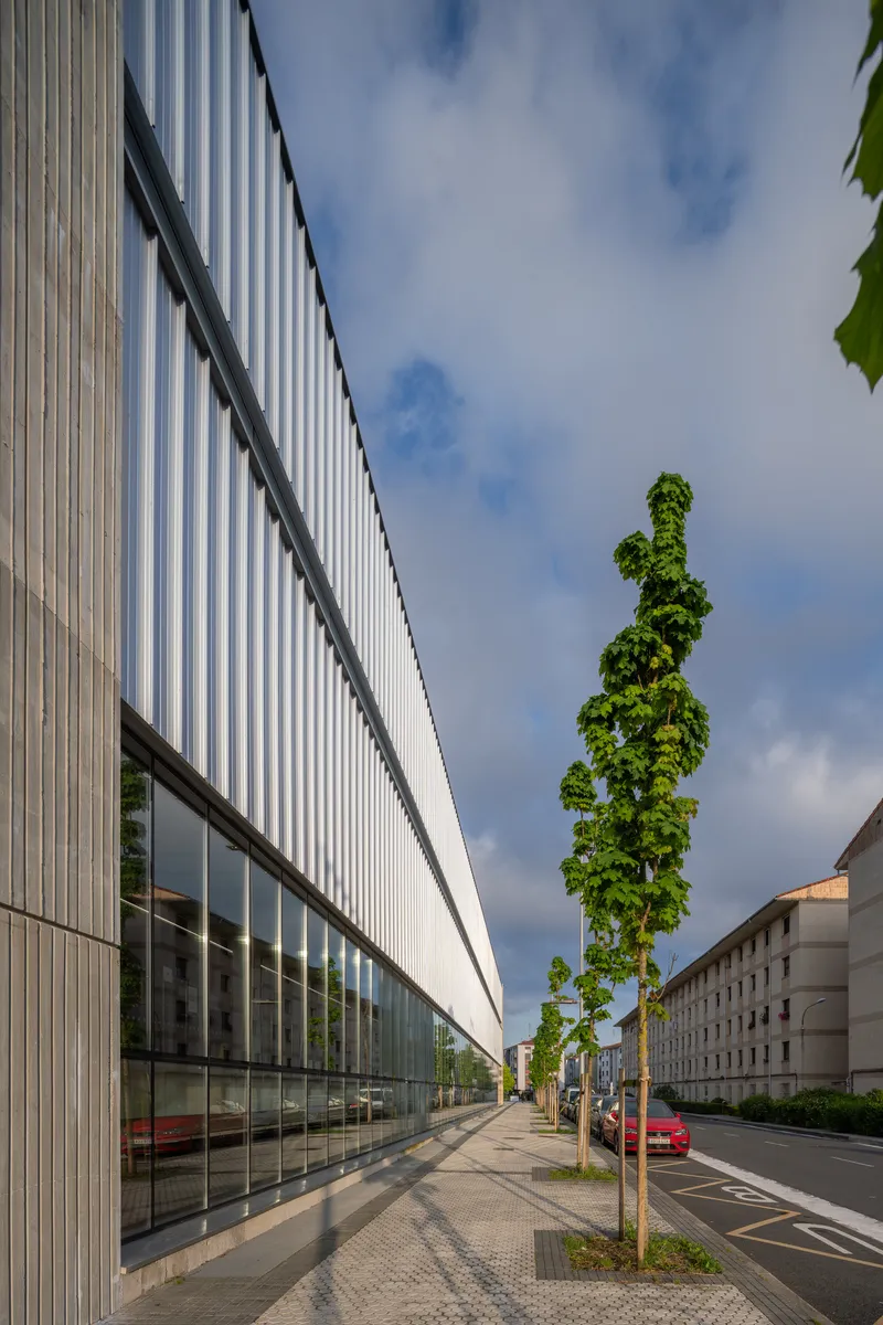 Street view of the ribbed metal facade with ground-level glazing and young trees along the sidewalk