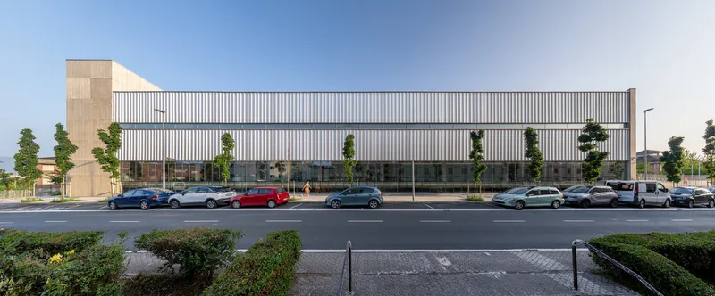 Long horizontal volume with vertical metal cladding facing a parking lot under partly cloudy skies