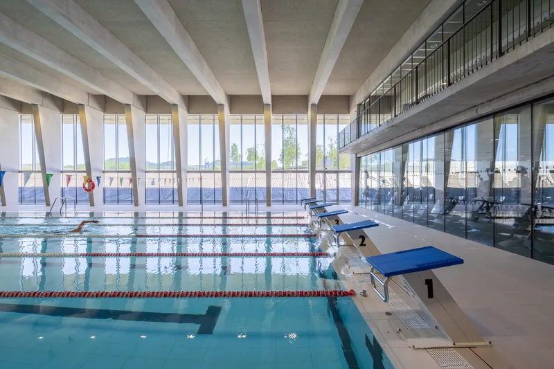 Competition pool with starting blocks and angled concrete columns framing full-height glazing to outdoor terraces